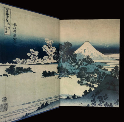 Woodblock print of Mount Fuji with trees and water, open book format.