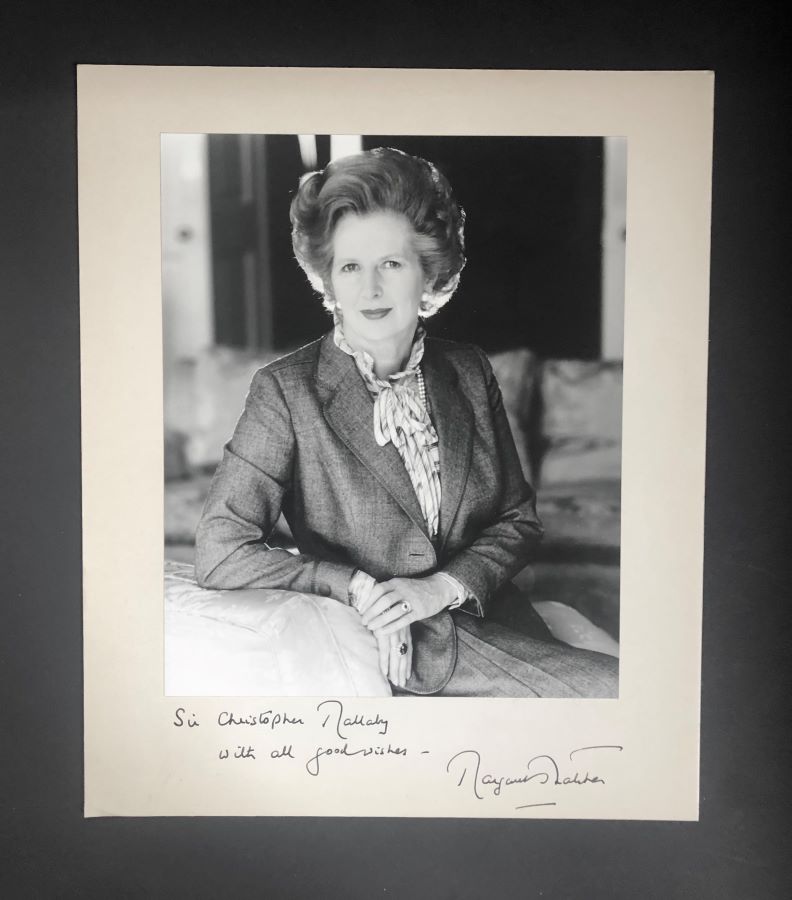 A black and white portrait photograph of Margaret Thatcher with a handwritten inscription and signature.
